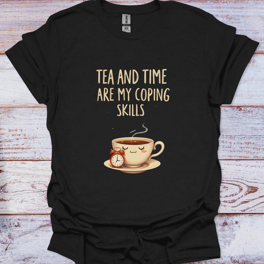 Black t-shirt with a graphic of a tea cup and clock, and text 'Tea and time are my coping skills' on a wooden surface.