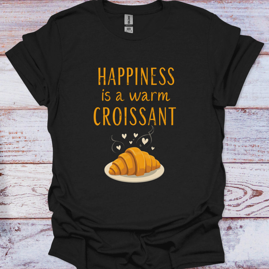 Black t-shirt with 'Happiness is a warm croissant' text and croissant graphic on a wooden surface