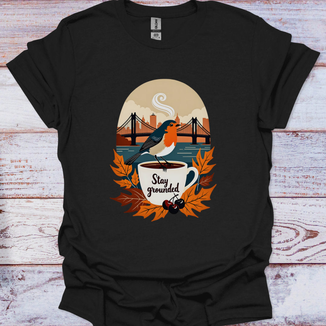 Black t-shirt with a graphic of a bird on a cup with 'Stay grounded' text, surrounded by leaves and a cityscape.