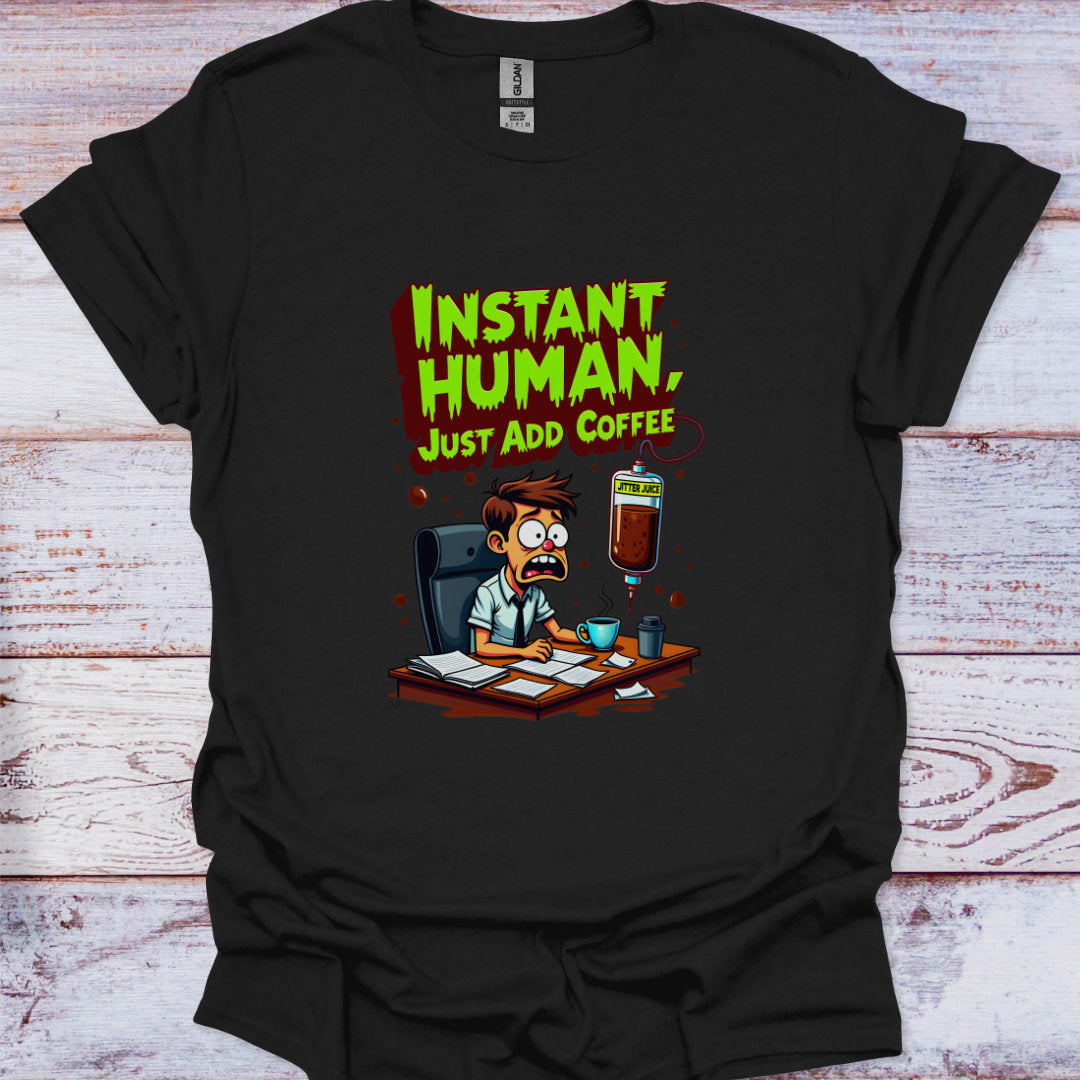 Black t-shirt with cartoon design and text 'Instant Human, Just Add Coffee' on a wooden surface.