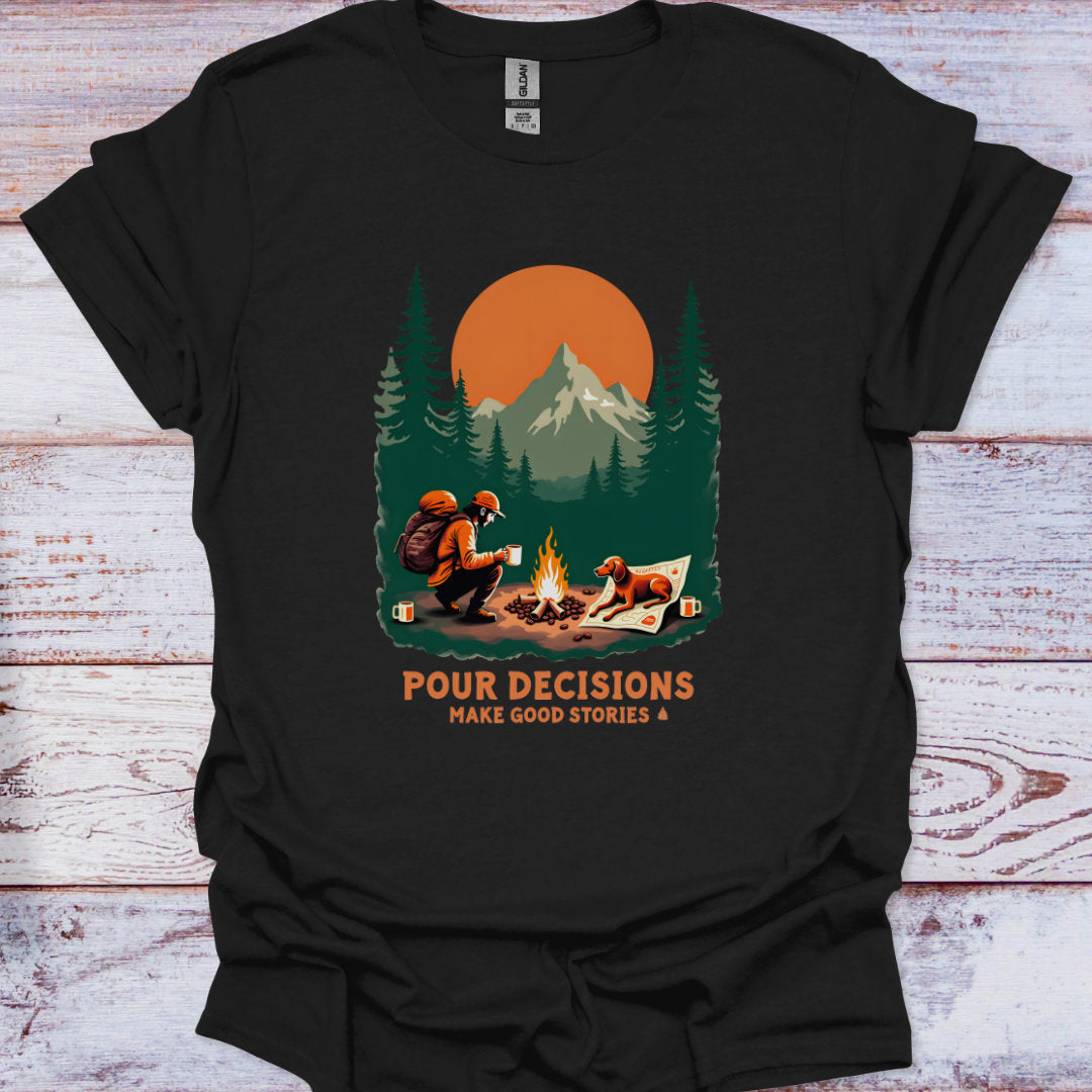 Black t-shirt with a graphic of man and his dog by a campfire and mountains, with text 'Pour Decisions Make Good Stories' on a wooden surface.