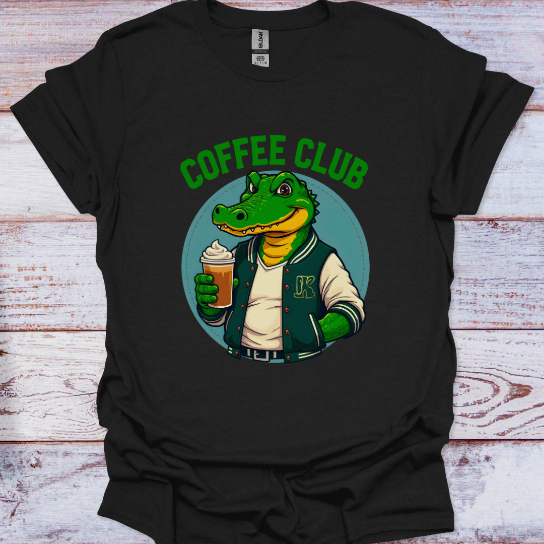 Black t-shirt with a graphic of a crocodile in a coffee club theme on a wooden surface.