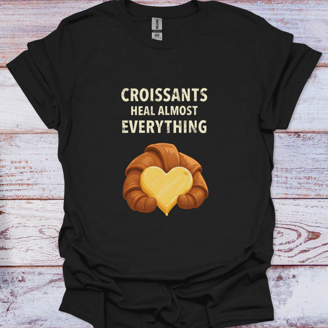 Black t-shirt with a croissant graphic and text 'Croissants heal almost everything' on a wooden surface.