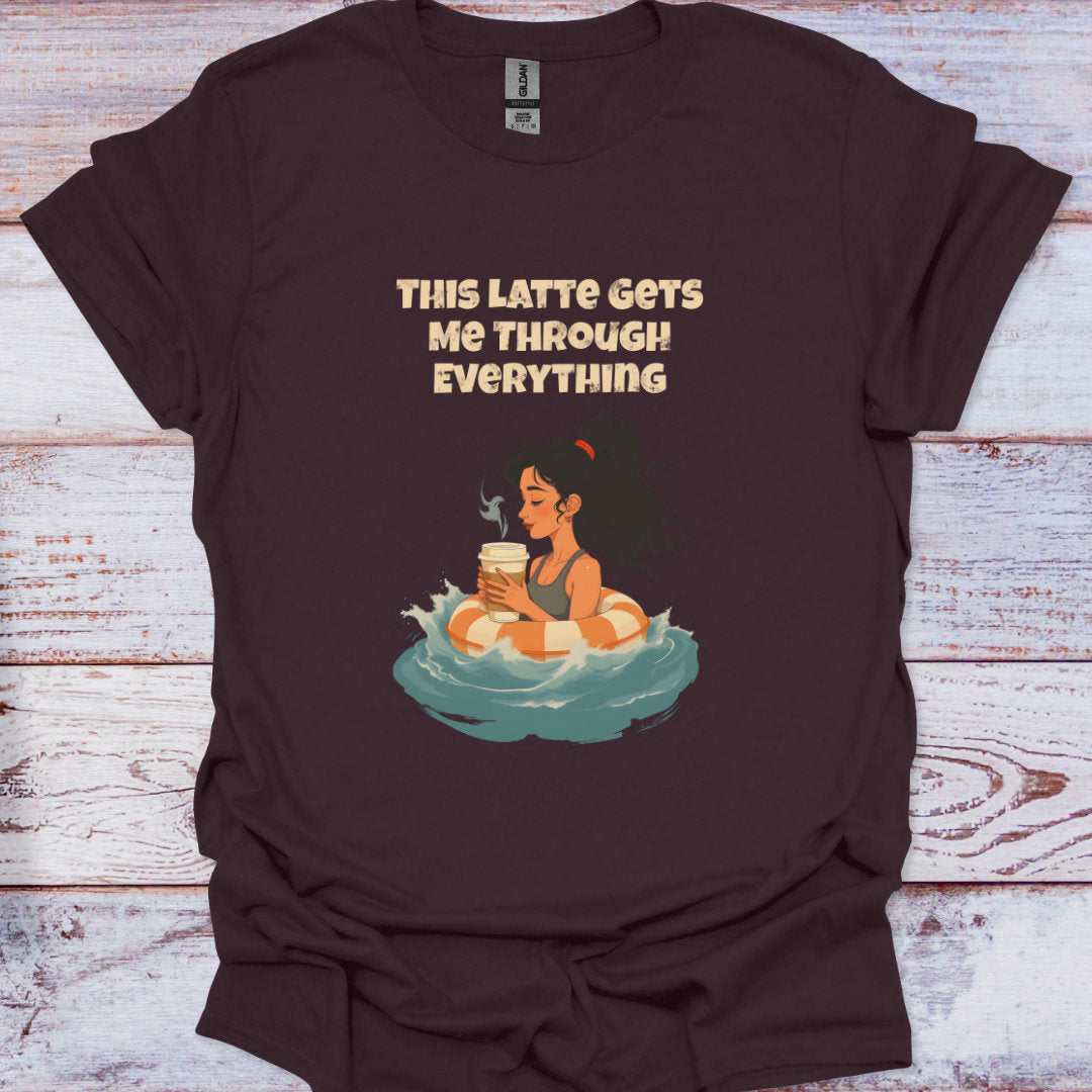 Brown t-shirt with graphic of a character in a hot tub holding a coffee cup and text 'This Latte Gets Me Through Everything' on a wooden surface.