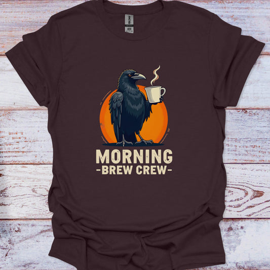 Brown t-shirt with a crow holding a coffee cup and 'Morning Brew Crew' text on a wooden surface