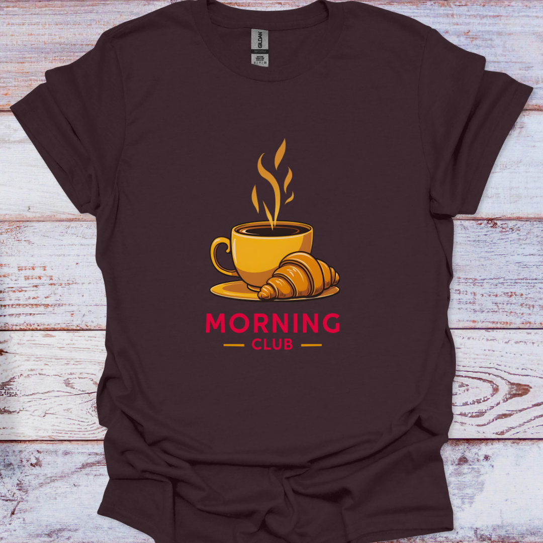 Brown t-shirt with a coffee cup and croissant graphic and 'Morning Club' text on a wooden surface.