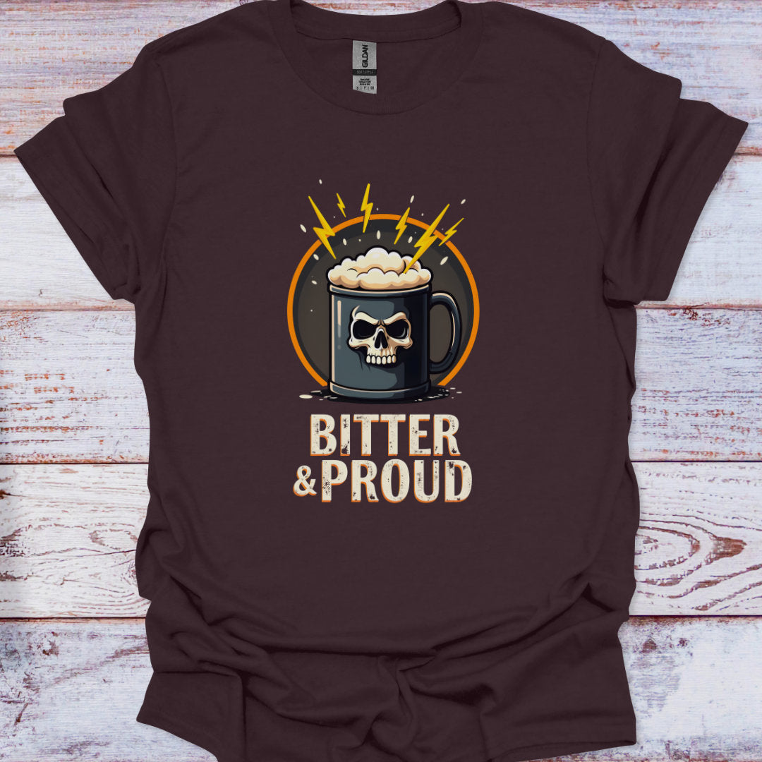Brown t-shirt with a graphic of a skull in a mug and 'Bitter & Proud' text on a wooden surface.