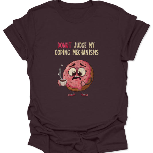 Graphic t-shirt on a dark chocolate brown background featuring a nervous pink-frosted donut holding a steaming coffee cup with the text "Donut Judge My Coping Mechanisms."