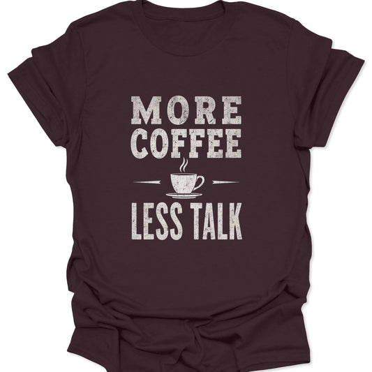 Dark brown t-shirt featuring a central white typographic graphic demanding 'MORE COFFEE LESS TALK' with a small, stylized steam cup illustration.