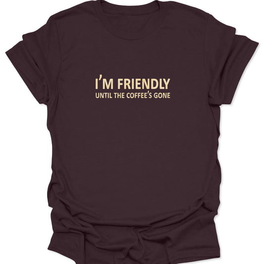A dark chocolate brown t-shirt with the minimalist quote "I'M FRIENDLY UNTIL THE COFFEE'S GONE" printed in a cream-colored serif and sans-serif font mix.