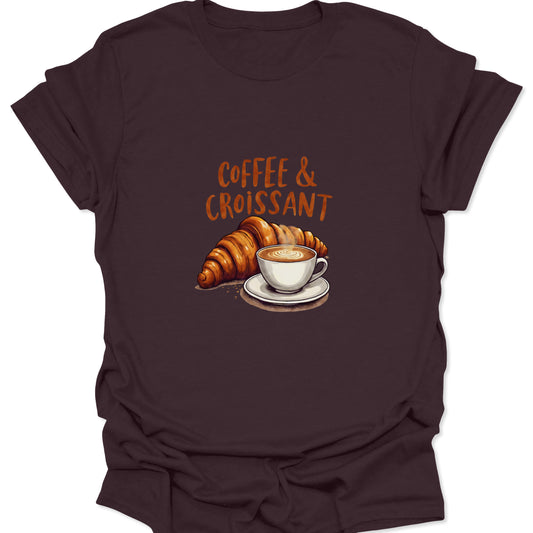 Dark brown t-shirt featuring the classic breakfast pairing: a rich coffee drink in a white cup and a large flaky croissant, with bold, rustic lettering. Essential bakery graphic tee.