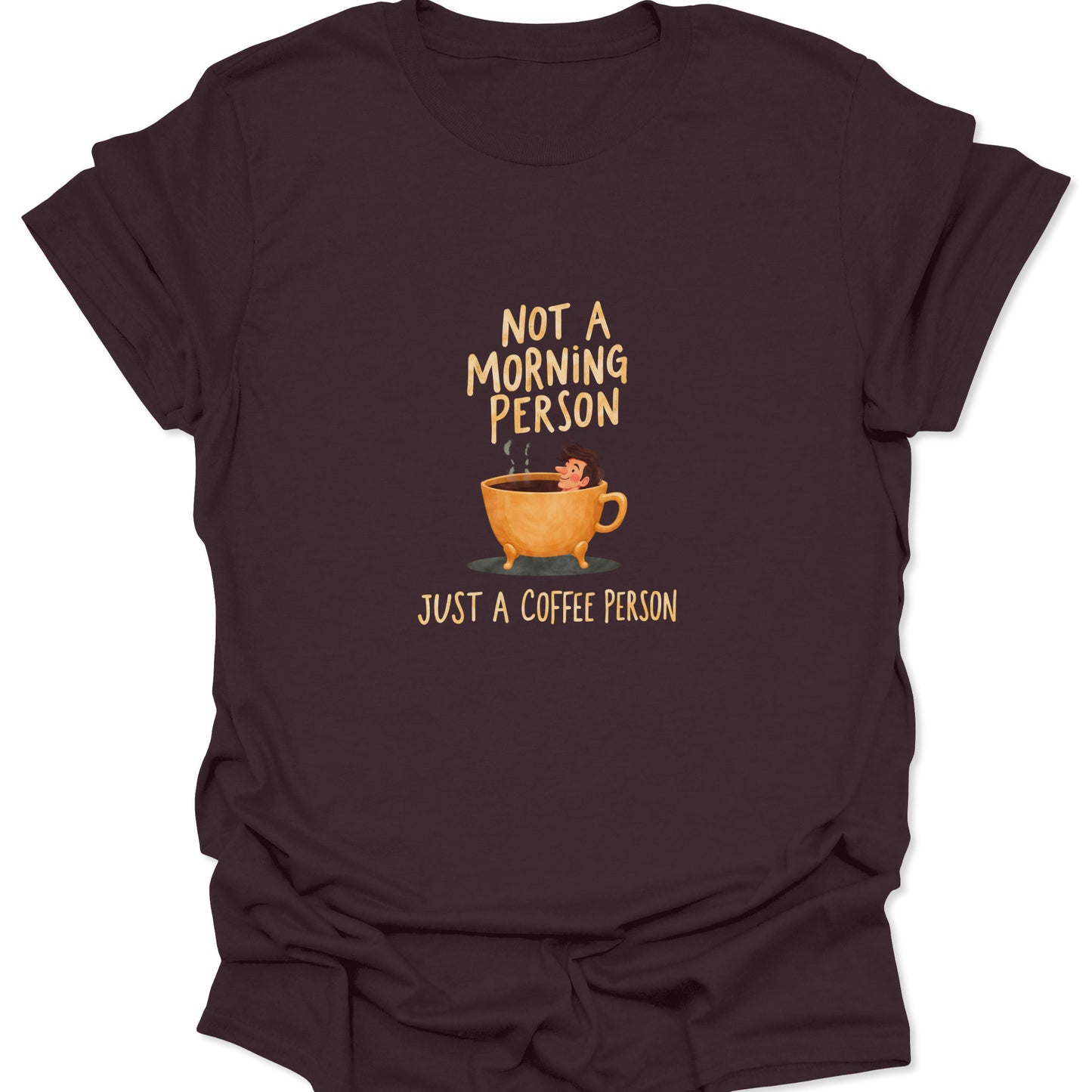 Dark brown t-shirt with a vintage-style coffee graphic: a tiny figure submerged in an overflowing, hot coffee mug. Text reads: "NOT A MORNING PERSON, JUST A COFFEE PERSON."