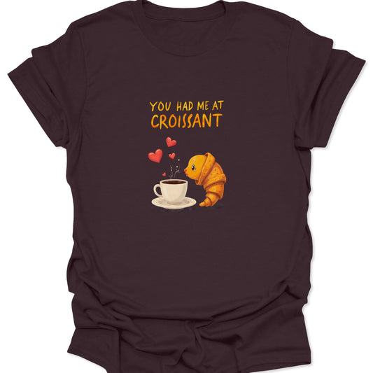 Dark chocolate brown shirt featuring a fun, vibrant graphic of a cartoon croissant passionately embracing a coffee mug, surrounded by hearts and 'You Had Me at Croissant' text.