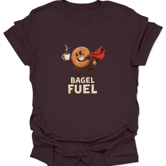 Dark chocolate brown t-shirt featuring a dynamic illustration of a super-powered bagel and coffee combination with dramatic red cape detail, text reads "BAGEL FUEL."