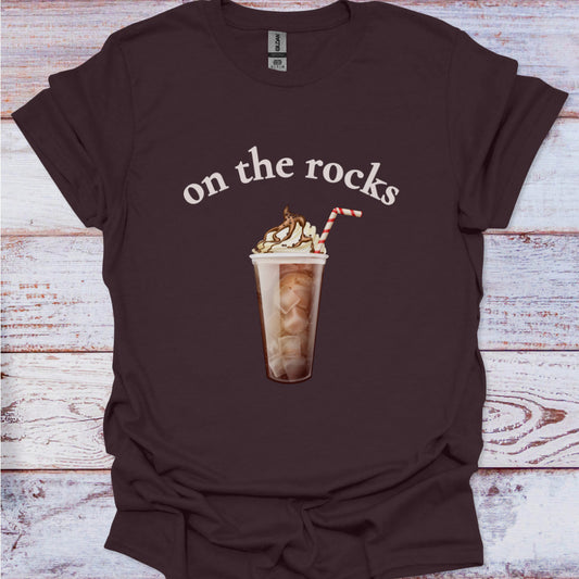 Brown t-shirt with a graphic of an iced coffee and text 'on the rocks' on a wooden surface.