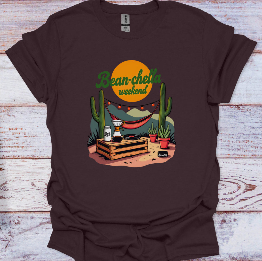 Brown t-shirt with a graphic design featuring cacti, a beer can, and a coffee cup on a wooden surface.