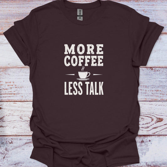 Dark brown t-shirt featuring a central white typographic graphic demanding 'MORE COFFEE LESS TALK' with a small, stylized steam cup illustration.
