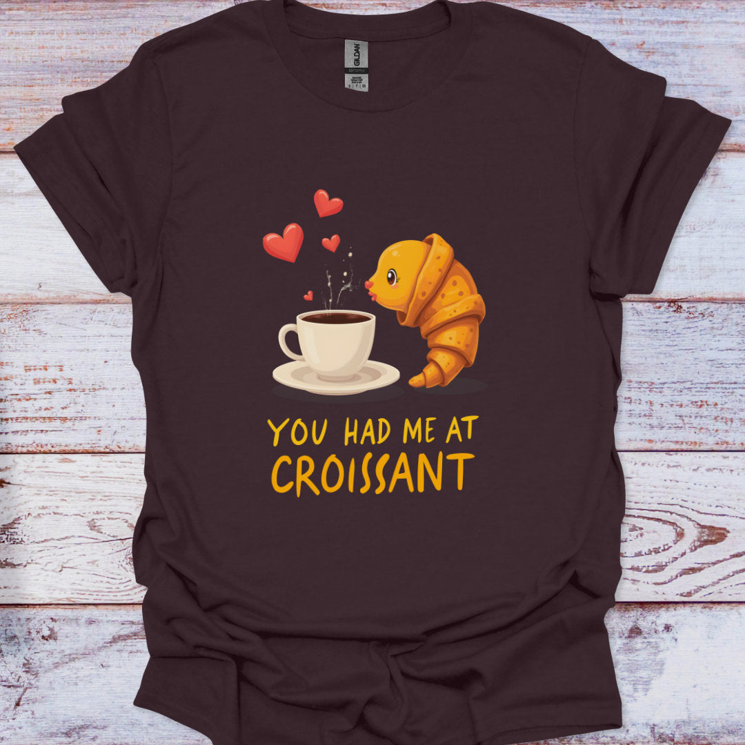 Brown t-shirt with a croissant and coffee cup graphic and 'You Had Me at Croissant' text on a wooden surface.