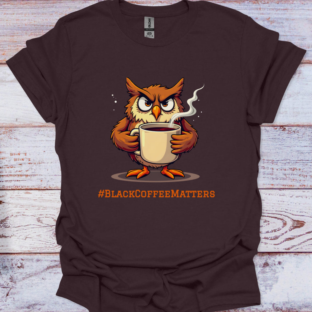 Brown t-shirt with an owl holding a coffee cup and '#BLACKCOFFEEMATTERS' text on a wooden surface.