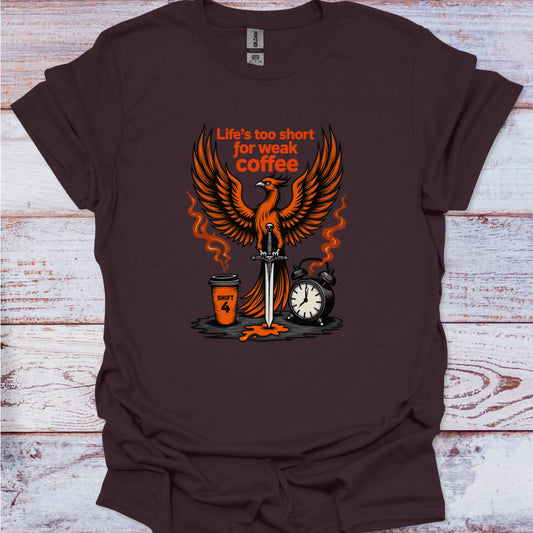 Brown t-shirt with a graphic design featuring an phoenix, coffee cup, sword, and alarm clock on a wooden surface.