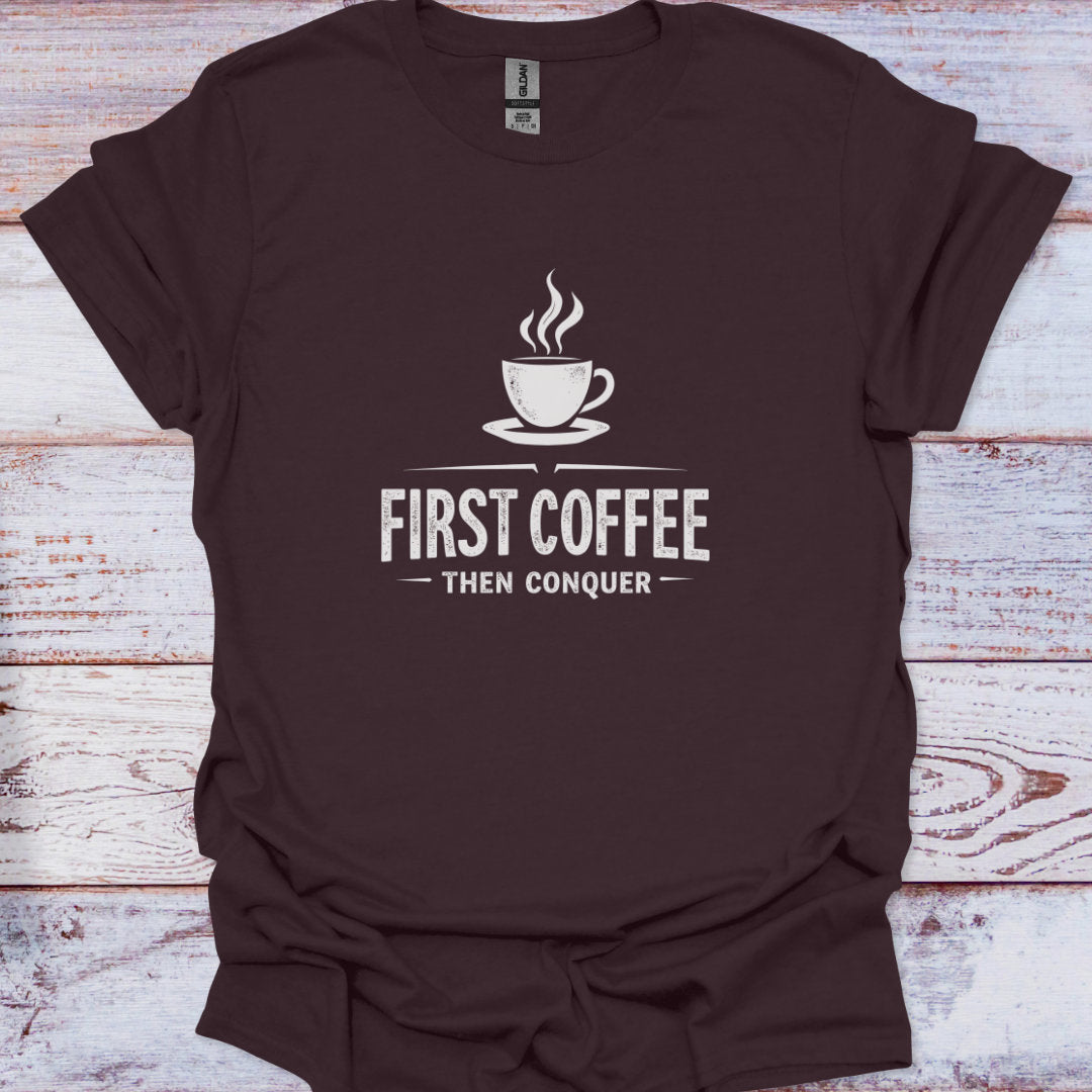 Brown t-shirt with 'First Coffee Then Conquer' text and coffee cup graphic on a wooden surface