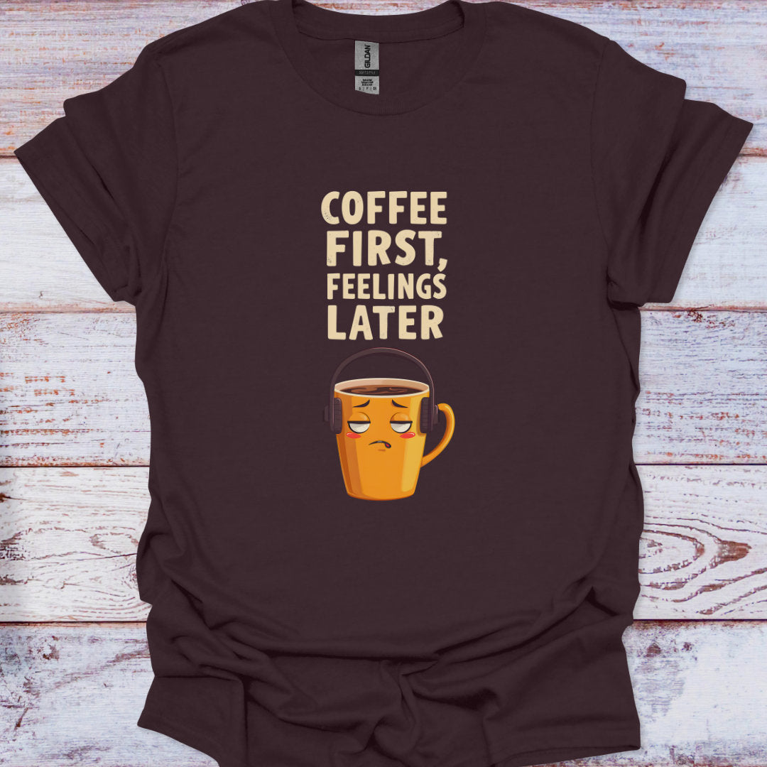 Brown t-shirt with a coffee cup graphic and text 'Coffee First, Feelings Later' on a wooden surface.