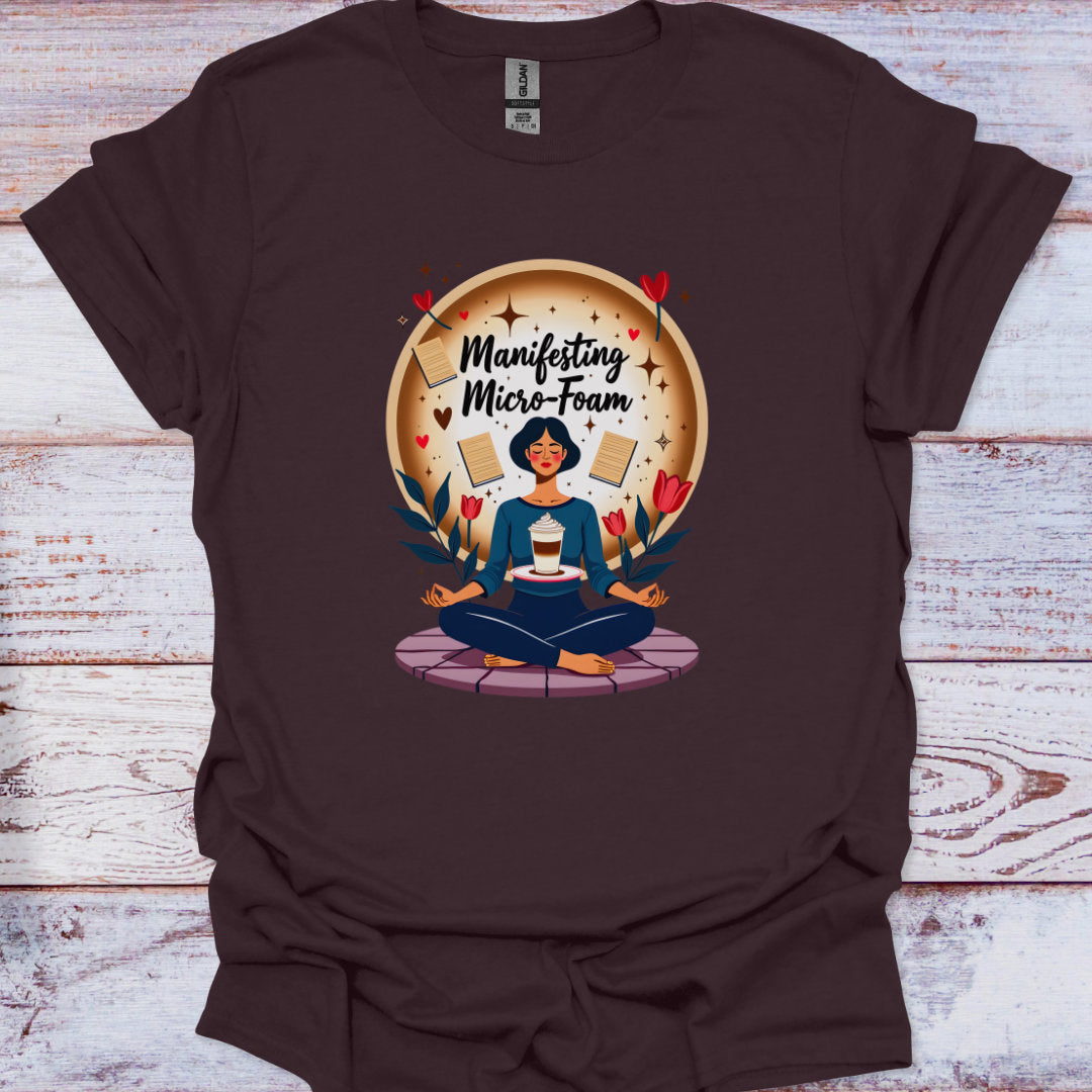 Brown t-shirt with a graphic of a person meditating and text 'Manifesting Micro-Foam' on a wooden surface.