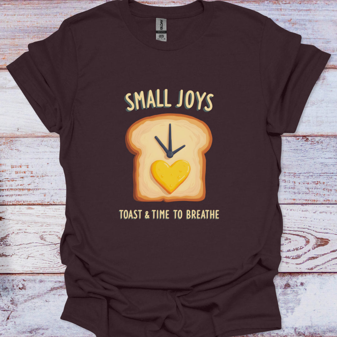 Brown t-shirt with a graphic of toast and a heart, text 'Small Joys Toast & Time to Breathe' on a wooden surface.
