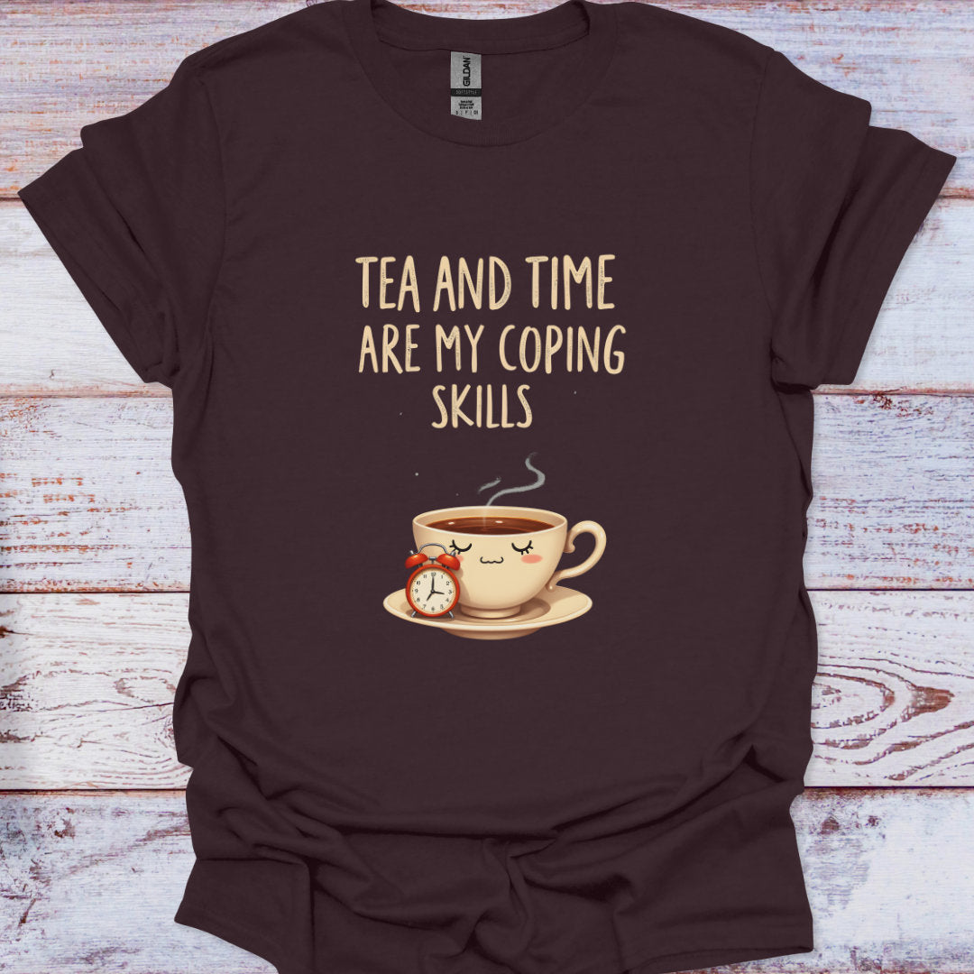 Brown t-shirt with a graphic of a coffee cup and clock, and text 'Tea and time are my coping skills' on a wooden surface.
