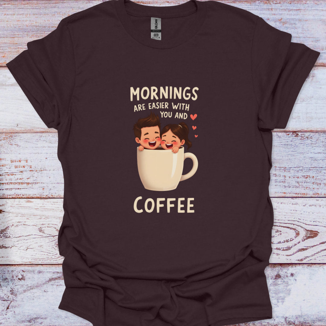 Brown t-shirt with a graphic of two people in a coffee cup and text 'Mornings are easier with you and coffee' on a wooden surface.