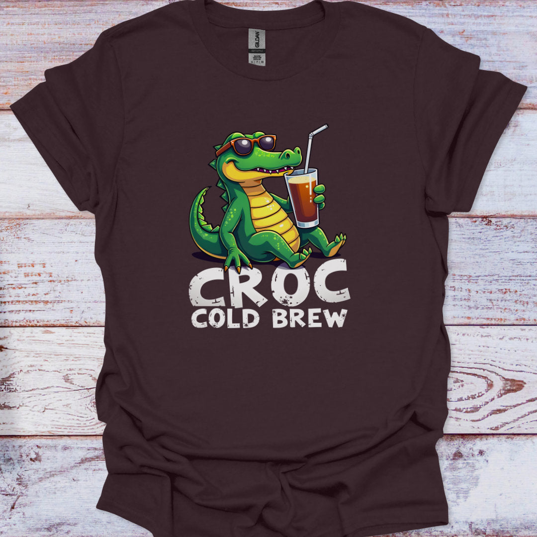 Brown t-shirt with a green crocodile holding a cup labeled 'Croc Cold Brew' on a wooden surface.