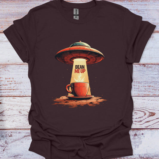 Brown t-shirt with a UFO and coffee cup graphic and 'Bean Me Up' text on a wooden surface.