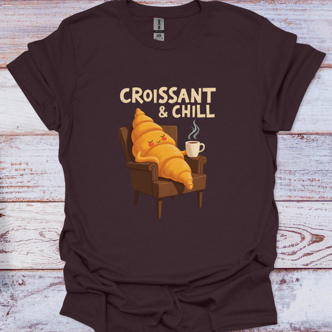 Brown t-shirt with a cartoon croissant character and 'Croissant & Chill' text on a wooden surface.