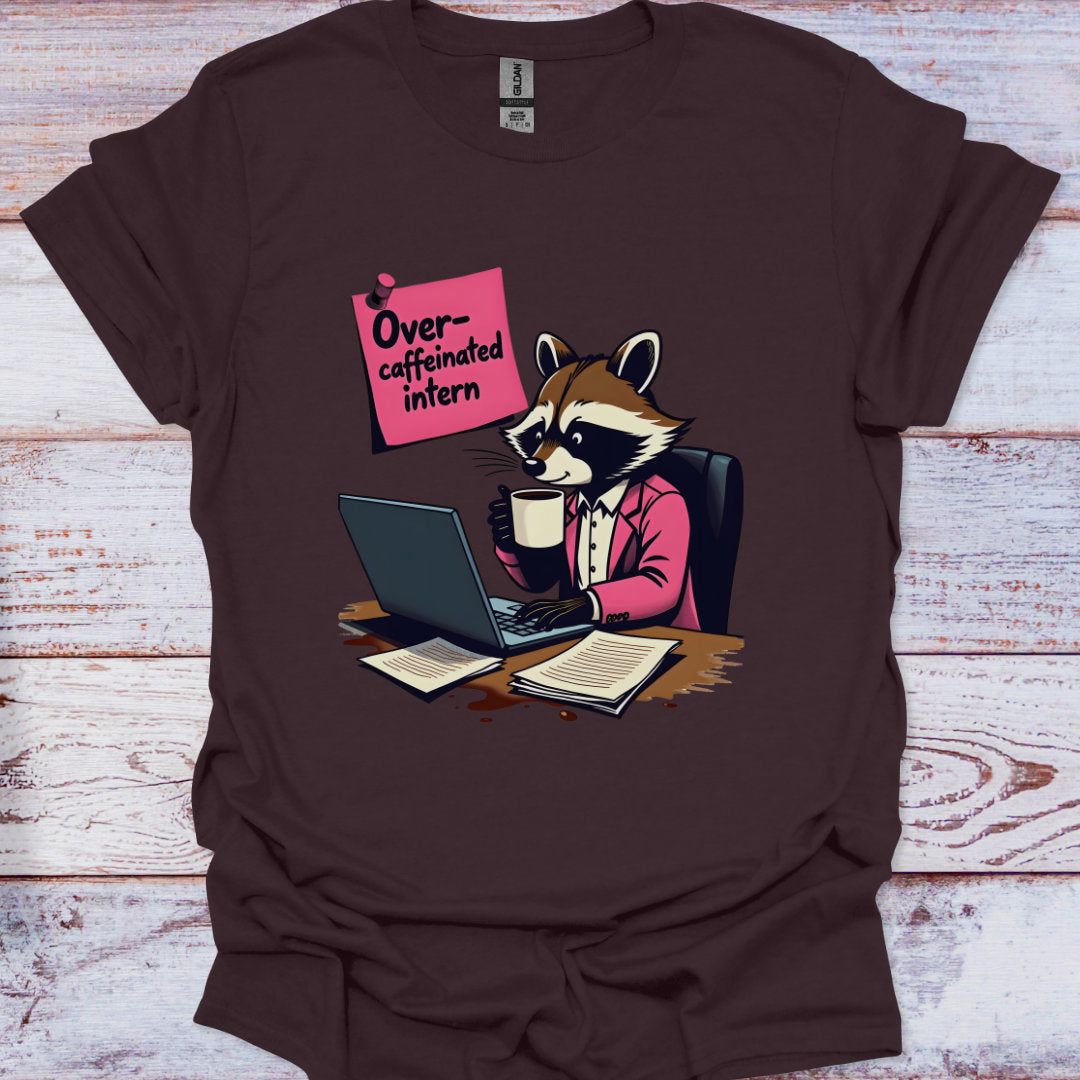 Brown t-shirt with a raccoon graphic and text 'Overcaffeinated intern' on a wooden surface.