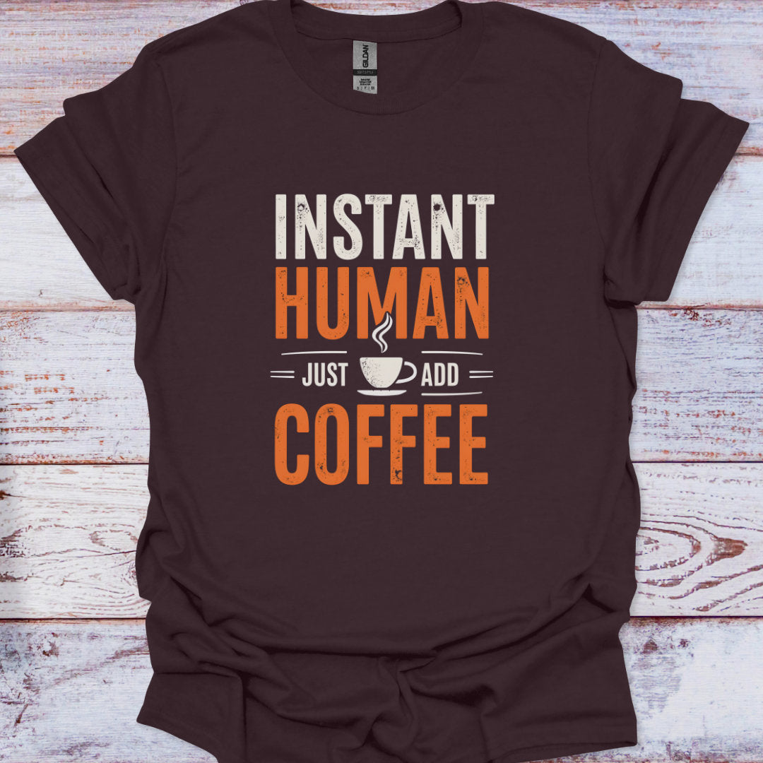 Brown t-shirt with 'Instant Human, Just Add Coffee' text on a wooden surface