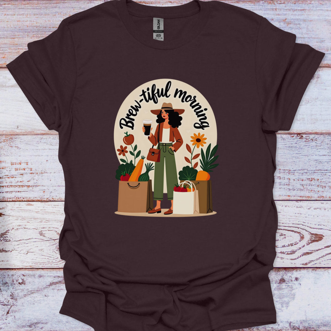 Brown t-shirt with a graphic of a woman holding a coffee cup and shopping bags, with 'Brew-iful morning' text, on a wooden surface.