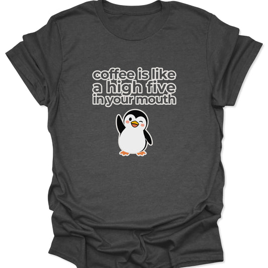 A dark heather gray t-shirt featuring a white and yellow cartoon penguin winking and waving below the text "coffee is like a high five in your mouth" in a bold, rounded font.