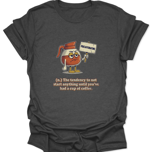 A dark heather gray graphic t-shirt featuring a cartoon coffee carafe with a grumpy face holding a "PROCAFFEINATING" sign above a dictionary-style definition.