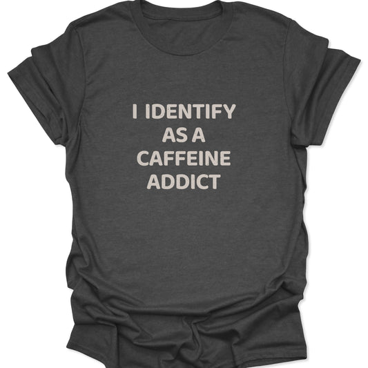 A dark heather gray shirt with a high-contrast graphic reading "I IDENTIFY AS A CAFFEINE ADDICT" in a textured block font.