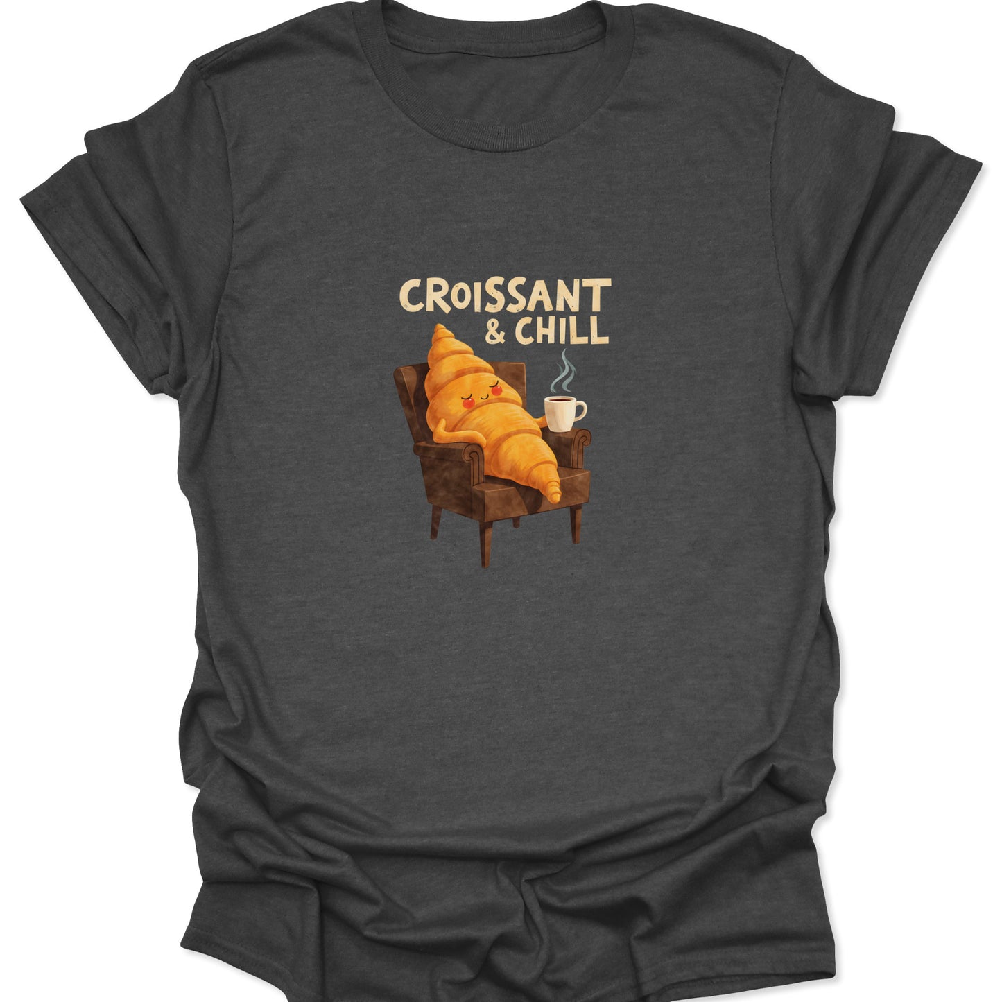 Witty food-themed graphic tee. Content croissant character lounging in a chair with coffee and 'CROISSANT & CHILL' text printed on a dark heather gray fabric.

