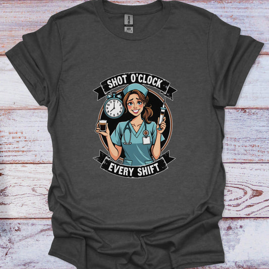 Dark gray t-shirt with a graphic of a nurse holding a clock and a bottle, text 'Shot O'Clock Every Shift', on a wooden surface.