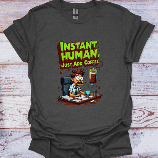 Gray t-shirt with a cartoon character and text 'Instant Human, Just Add Coffee' on a wooden surface.