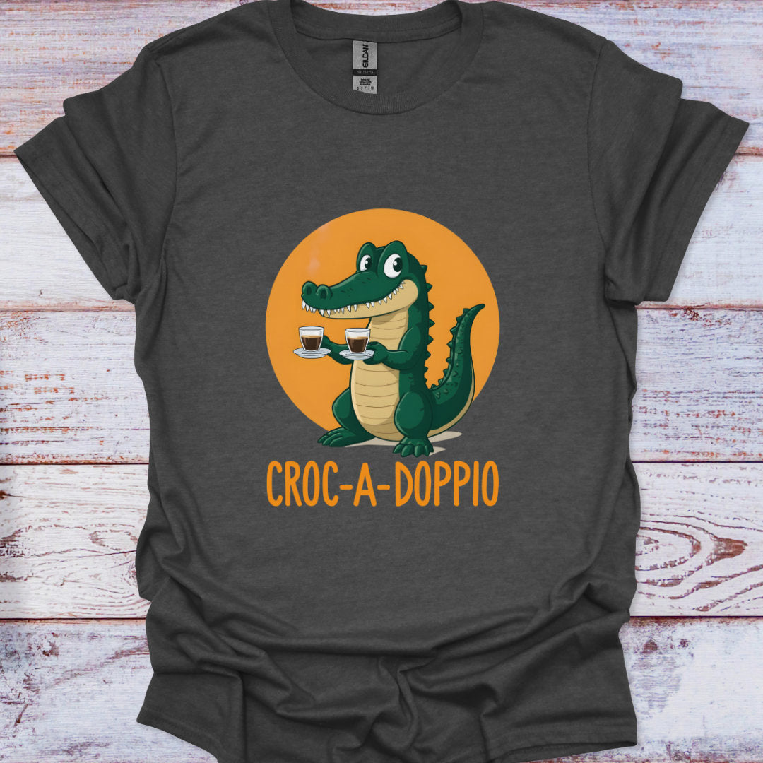 Dark gray t-shirt with a cartoon crocodile holding two cups on an orange background, text 'Croc-a-Doppio' on a wooden surface.