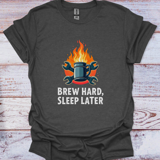 Dark gray t-shirt with a graphic of a mug on fire and text 'Brew Hard, Sleep Later' on a wooden surface.