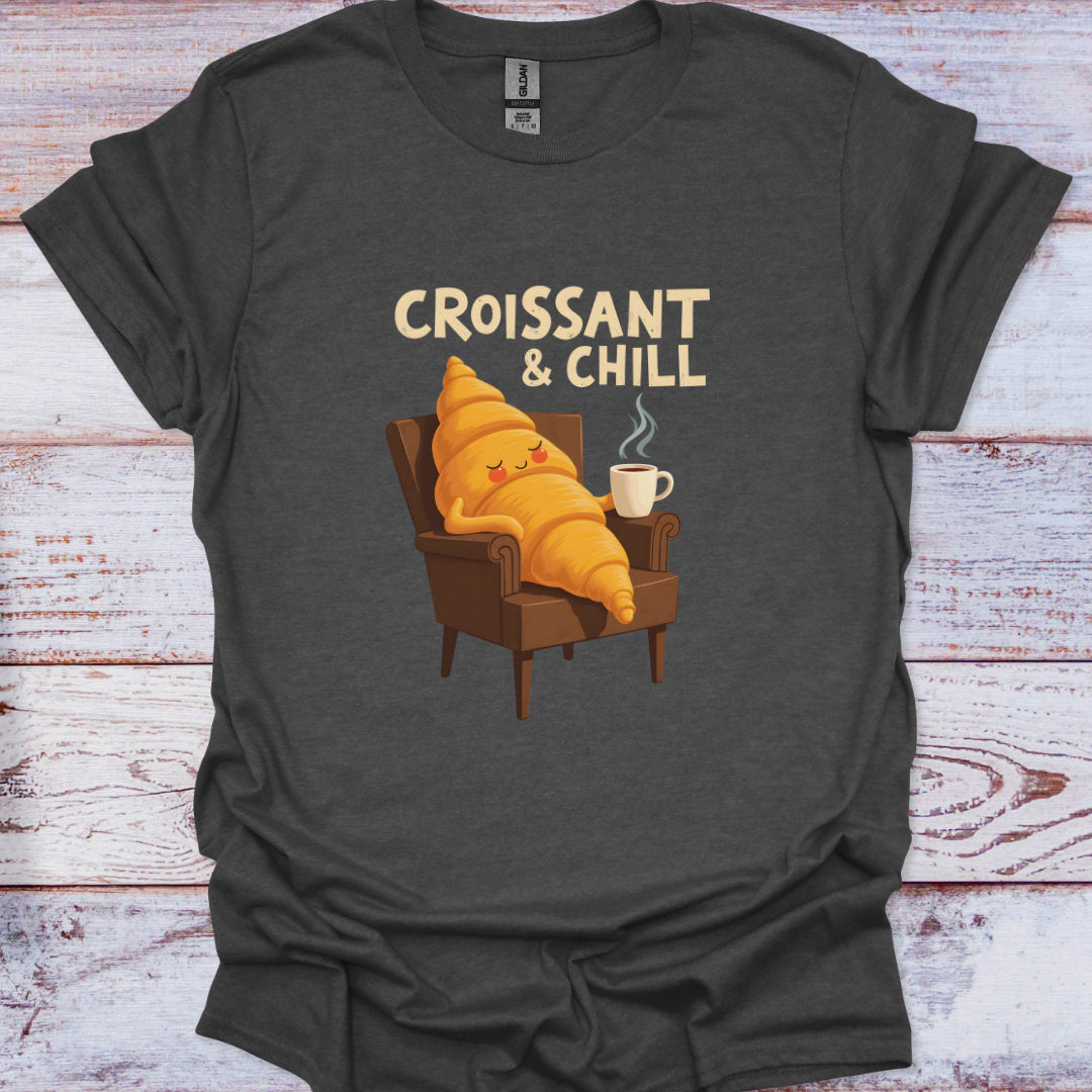 Dark gray t-shirt with a cartoon croissant character and 'Croissant & Chill' text on a wooden surface.