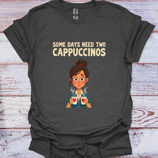 Dark gray t-shirt with cartoon character holding coffee cups and text 'Some days need two Cappuccinos' on a wooden surface.
