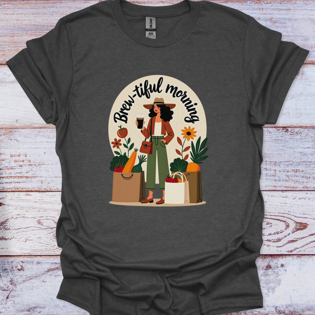 Dark gray t-shirt with a graphic of a woman holding a coffee cup and shopping bags, with 'Brew-iful morning' text, on a wooden surface.