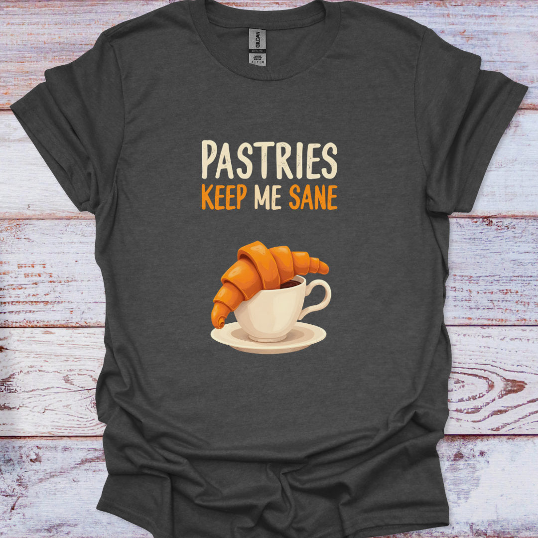 Dark gray t-shirt with a graphic of a croissant and coffee cup and text 'Pastries Keep Me Sane' on a wooden surface.