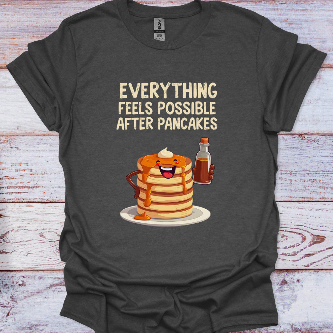 Dark gray t-shirt with a graphic of pancakes, syrup, and coffee cup with text 'Everything feels possible after pancakes' on a wooden surface.