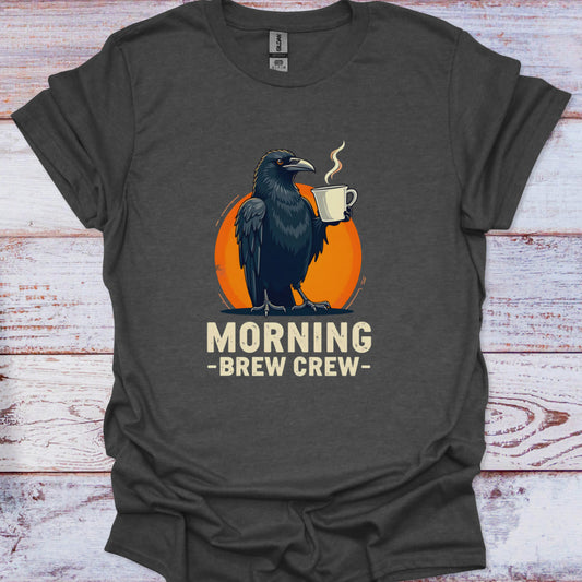Dark gray t-shirt with a crow holding a coffee cup and 'Morning Brew Crew' text on an orange circle, against a wooden background.